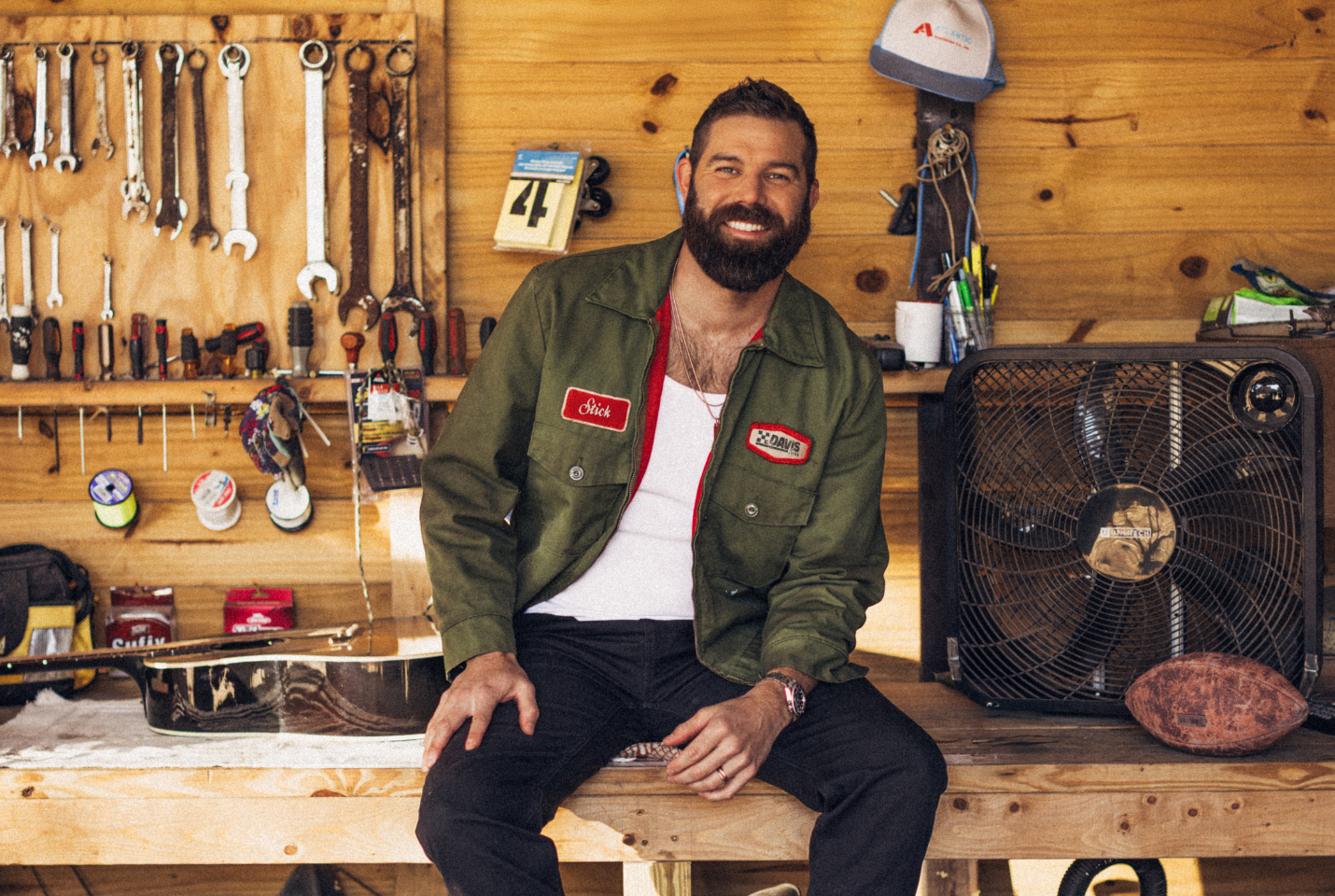 Man sitting on a workbench with tools behind him 